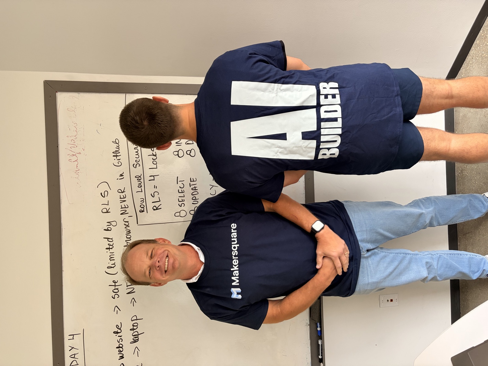 Two Cohort 1 builders at the whiteboard, one wearing the MakerSquare AI Builder shirt